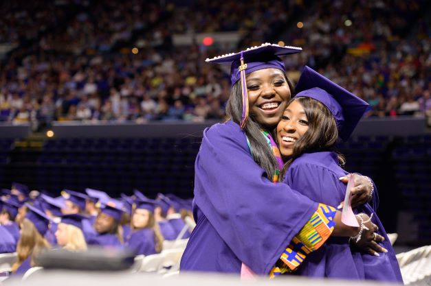 Two women hugging in caps and gowns at graduation ceremony. 