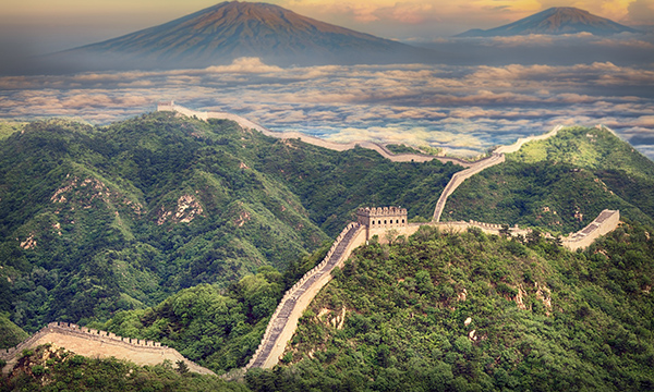 The Great Wall of China is surrounded by rolling green hills with mountains in the background.
