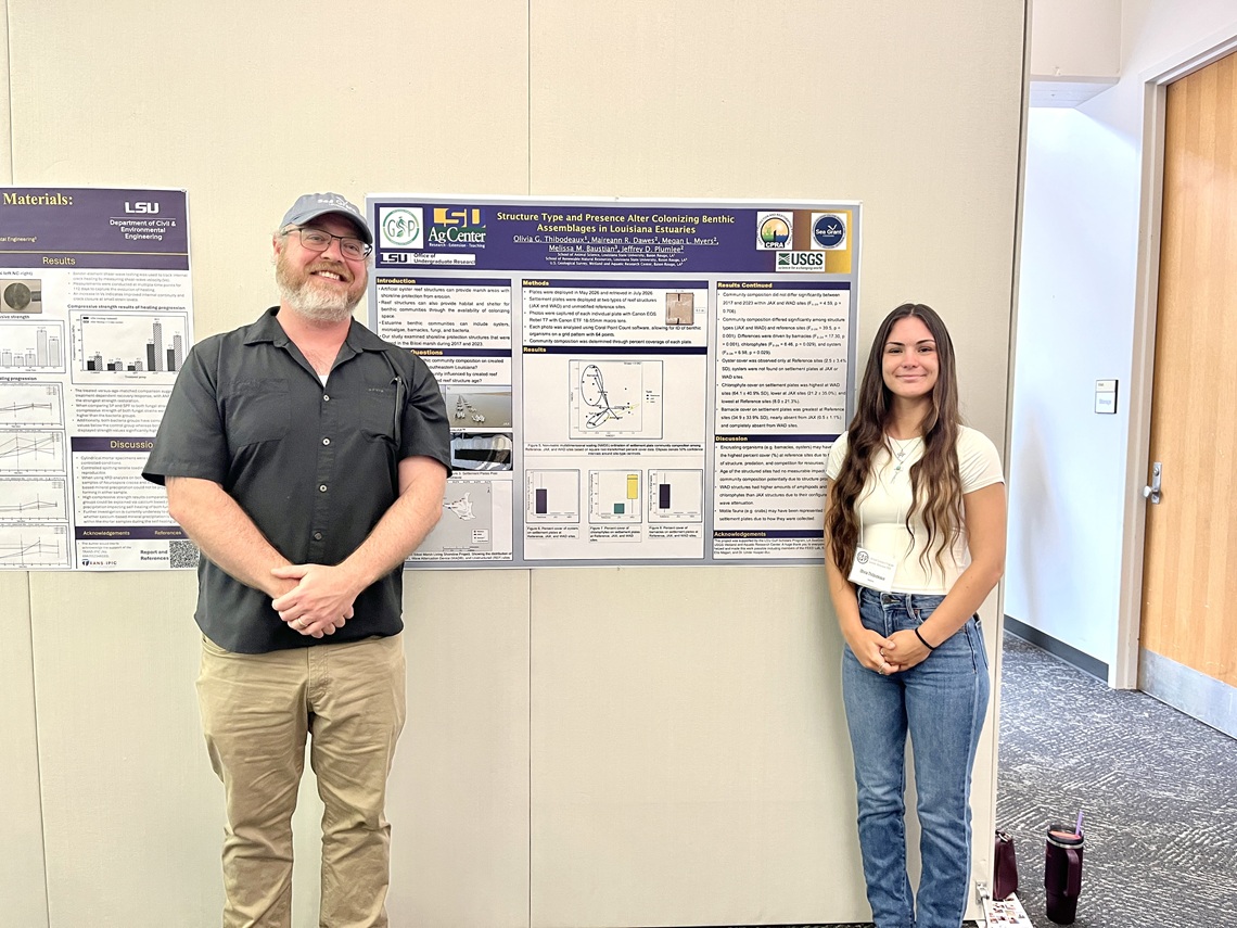 Student and faculty memeber stand beside a research poster at an academic poster session.