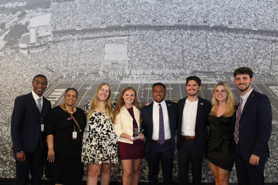 students and advisor stand in a line holding a trophy for student leader of the year